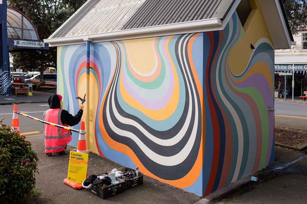 Artist Gina Kiel painting colourful, swirly mural on a public toilet in Island Bay.