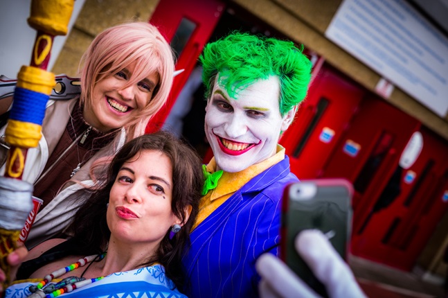 Person dressed up as Joker character and taking selfie with two fans.