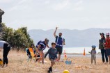 Adults and kids on the grass with many play objects, balls, hoops, cones, seats. The Wellington harbour is visible in the back ground.