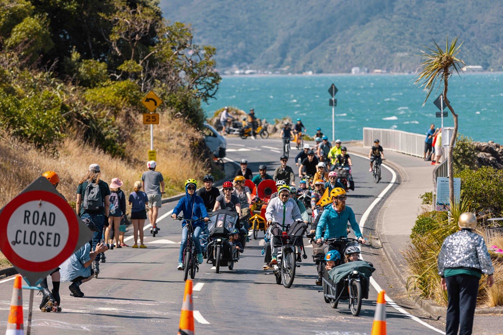 Shelly Bay road, showing a road closed sign on the left hand side of the image and road cones across the road. Behind the cones are a lot of bikes making their way along the road.
