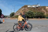 Two people standing with their bikes in front of the Wellington sign.