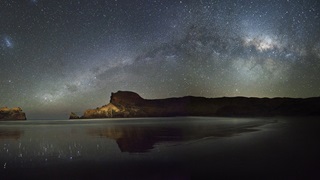 Landscape image of a beach with the night sky and lots of stars showing.