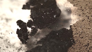 Still image taken from a video showing an abstract image of a rough-textured brown substance against a fine-grain white poweder. The brown substance is cracking dynamically, like dried mud.