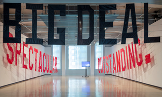 Banners by Elisabeth Pointon displaying the words 'Spectacular', 'Outstanding' and 'Big Deal' in large block letters hang in an gallery space with white walls.