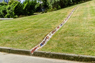 Physical artwork made of multicoloured ceramic tiles dug into a grass lawn to create a channel.