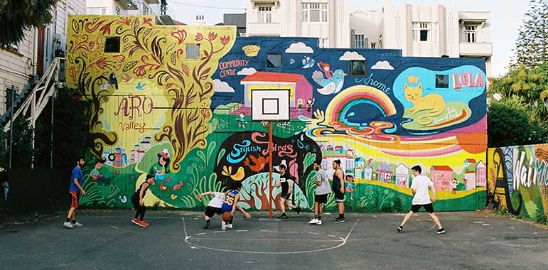 People playing basketball in front of a colourful mural.