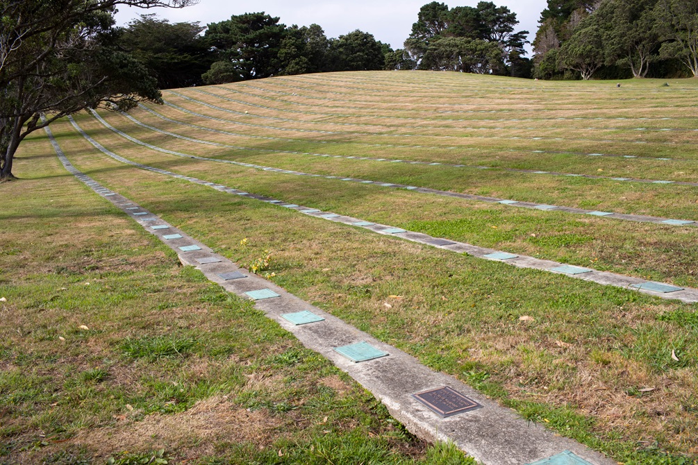 A large hilly lawn with memorial plaques in lines along the lawn;.