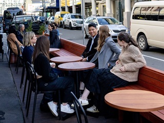 People relax in a parklet on Cuba Street, with small round wooden tables and a wood-lined bench seat.