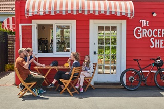 A family enjoying ice cream cones on a sunny day at a wooden table on the footpath outside of a cafe.
