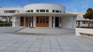 Photo of the exterior of Berhampore Centennial Community Centre, featuring a curved building painted white with wooden doors. 
