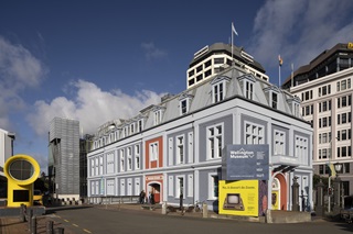 Exterior photo of Wellington Museum on the waterfront. A sign promoting an exhibition is in the foreground.