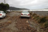 Cars parked among the debris on a stormy Ōwhiro Bay road