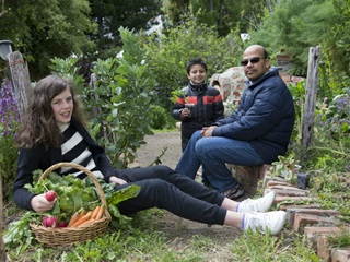 People sitting in a garden with a basket of fruit and vegetables.