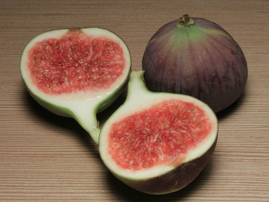 Two figs on a table, one sliced in half showing the inside.