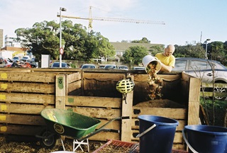 A person pouring food waste into a wooden compost bin.