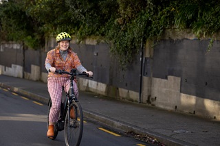 A woman wearing bright colours and a yellow helmet cycling on a road, heading towards the viewer.