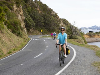 A person cycling along a coastal road with other cyclists following in the background. 