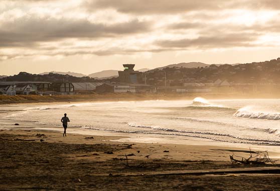 Person running at Lyall Bay beach at sunset time.
