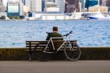 A person sitting on a bench in front of the sea in Oriental Parade, and a bicycle resting on the bench. 
