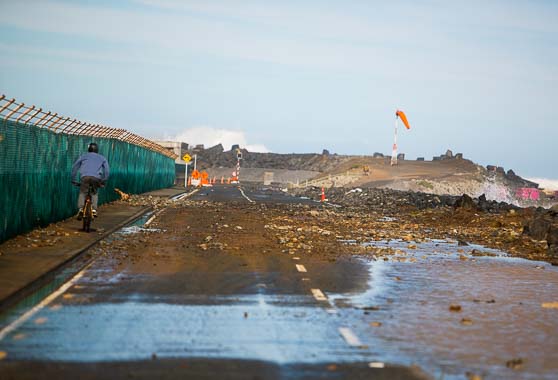 Cyclist passing next to debris near Wellington Airport caused by a storm surge.