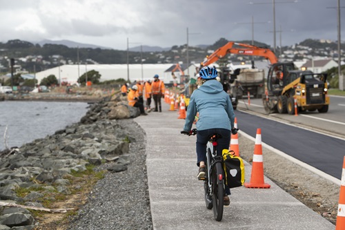 A woman cycling along Cobham Drive lined with road cones and construction workers in the distance.