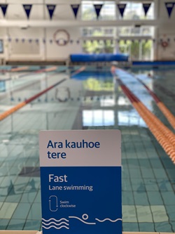 The fast swimming lane sign at Tawa Pool in te reo Māori with the swimming pool and lanes in the background.