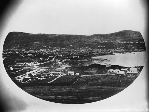 A historical photograph of Wellington harbour, with small settlements around the shoreline.