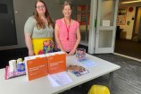 Two smiling women in lovely bright clothing standing at a table with information about Skinny Broadband and lollies on offer.