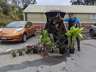 A gardener and a police officer giving a high-five in front of a car with plants that were stolen and then returned.