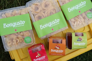 Thee packets of Bongusto Pasta and three pasta sauces displayed on a plastic yellow lid on grass. 