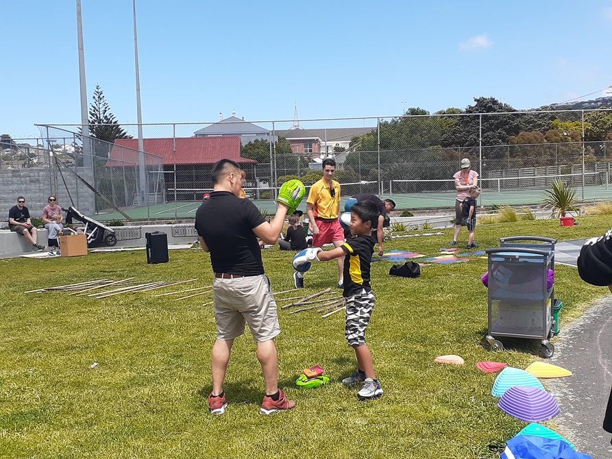 A man and a young kid practicing their boxing moves in gloves on the grass outside Waitohi.
