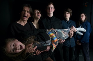 Five teenagers standing in a row, holding a sixth teen horizontally, all making funning faces at the camera. The photo is of Wellington jazz band, Mel Stevenson.