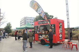 A red food truck, which serves Moroccan cuisine,  parked at the Harbourside Market, with customers waiting for their orders.