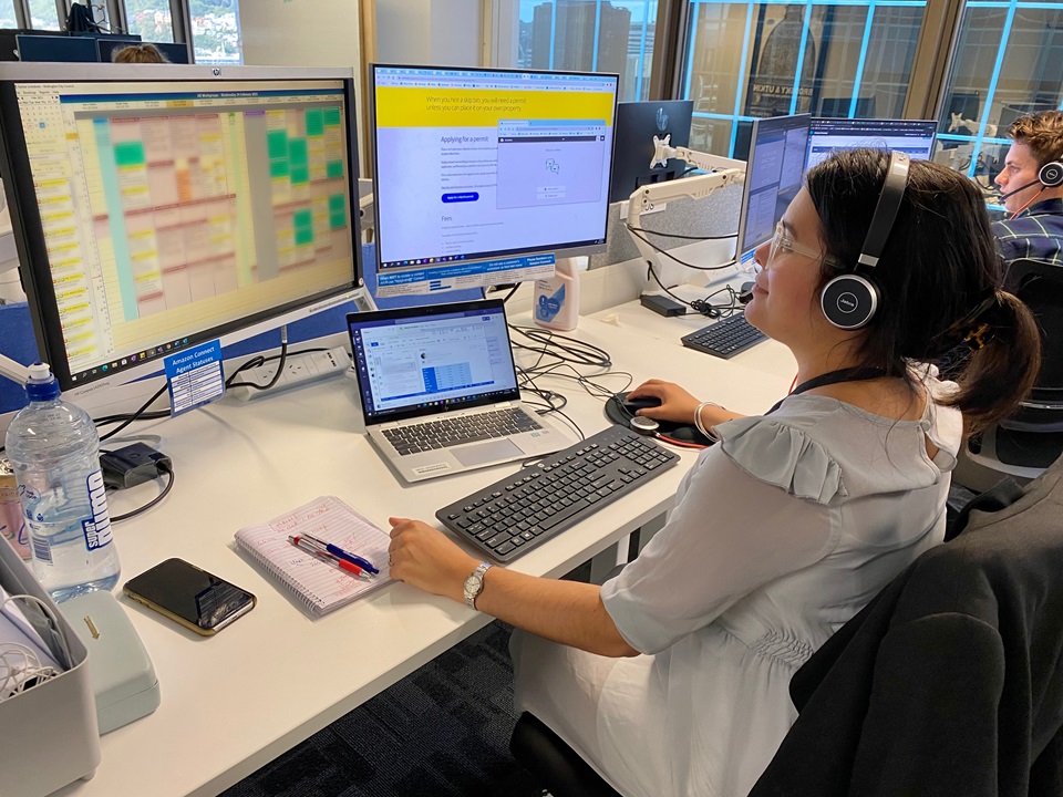 Contact Centre staff member Amber wearing a headset, at her desk with multiple computer screens open in front of her.
