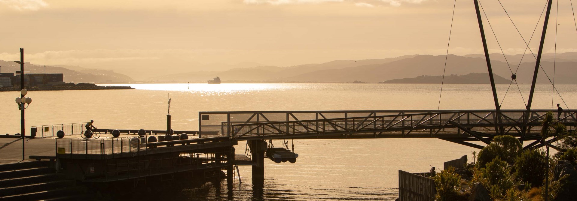 Wellington Harbour, doused in orange light as the sun comes up, looking out from the lagoon over the waterfront bridge towards Matiu/Somes Island.