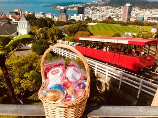 A basket of Easter eggs on a ledge with the iconic red cable car on its tracks with Wellington city and harbour in background.