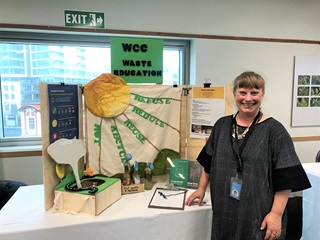 Jo Langford in a loose black and white speckled dress standing next to a waste reduction education table.