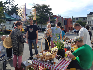Mark Noyes with a group of other people at a community event, standing around a table setup on a street with coffee, plants and food.