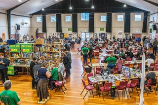 Photo of a hall full of tables with people playing board games on them.