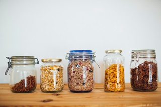A photograph of five differently sized glass jars containing different grains and cereals. 