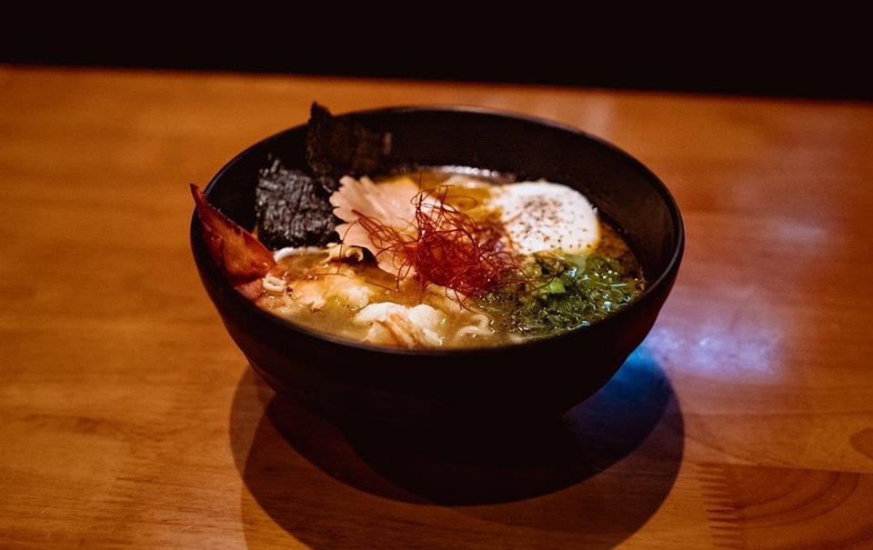 A black ceramic bowl full of ramen with noodles, crayfish, an egg and seaweed.