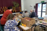 Six people who are IDEA Services volunteers spread out around two tables, working with rubber gloves preparing vegetables from carboard boxes.