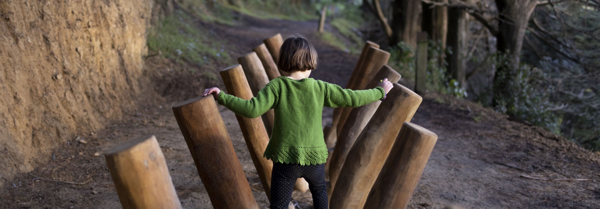 A young gir wearing a green jumper playing on a wooden play structure on Mount Victoria.