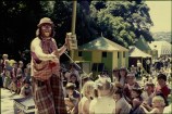A clown holding a tin can performs for a crowd of children from a stage.