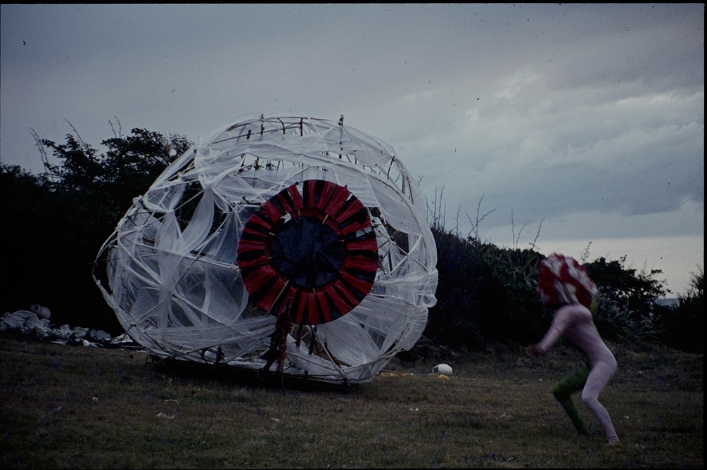 A giant eyeball made out of fabric wrapped around a frame outdoors on a field.