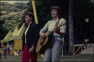 The Topp Twins perform outdoors with a guitar in the 1980s.