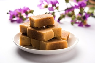Square pieces of mysore pak stacked on a white plate.