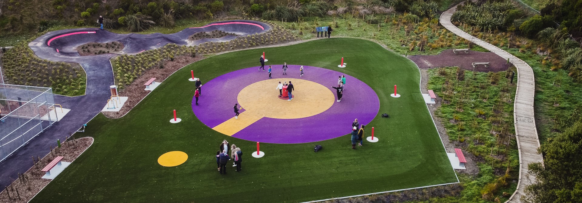 A birds eye view of the large yellow and purple Ki-O-Rahi pitch in the middle of a green grass field at Pukehuia Park in Newlands, with children playing.
