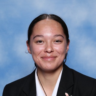 A professional school portrait headshot of a smiling teenage Kahurangi Douglas, with her dark hair tied behind her, wearing a white shirt and black blazer, and blue background.