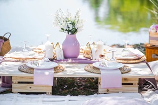 Old crates turned into a table, with lilac purple vase with flowers in the middle, and place settings on top of lilac clothe napkins.